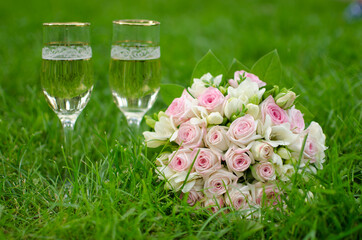 wedding bouquet on green grass and glasses with champagne