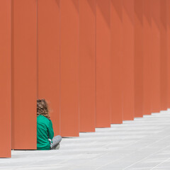 petite fille habillée de vert assise de dos devant un mur orange