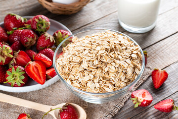 Healthy ingredients for breakfast. Homemade granola in open glass bowl, milk or yogurt, strawberries on table - health and diet concept