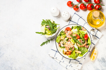 Seafood salad with fresh salad leaves, tomatoes and shrimps. Top view at white table.