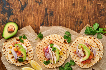 Mexican tacos with grilled chicken, avocado, corn kernels, tomato, onion, cilantro and salsa old wooden table. Traditional Mexican and Latin american street food. Top view.
