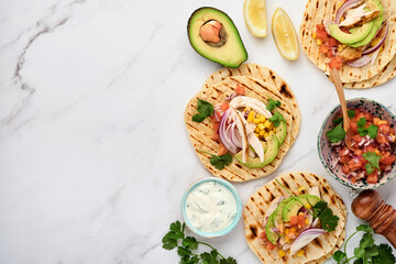 Mexican tacos with grilled chicken, avocado, corn kernels, tomato, onion, cilantro and salsa at white stone table. Traditional Mexican and Latin american street food. Top view.