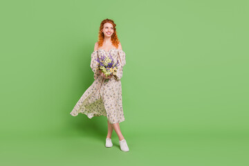 Full length photo of dreamy young happy woman look empty space hold flowers isolated on green color background