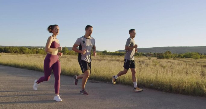 Multiethnic group of athletes running together on a panoramic countryside road. Diverse Team of joggers on morning training. 