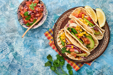 Mexican tacos with grilled chicken, avocado, corn kernels, tomato, onion, cilantro and salsa at blue stone table. Traditional Mexican and Latin american street food. Top view.
