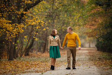 Happy couple on autumn walk outdoors. Two lovers in autumn park. Love and tender touch. Gentle hugs. Young man and woman in classic autumn colors outfit on a romantic date in a cozy park