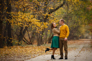 Fototapeta premium Happy couple on autumn walk outdoors. Two lovers in autumn park. Love and tender touch. Gentle hugs. Young man and woman in classic autumn colors outfit on a romantic date in a cozy park