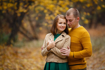 Happy couple on autumn walk outdoors. Two lovers in autumn park. Love and tender touch. Gentle hugs. Young man and woman in classic autumn colors outfit on a romantic date in a cozy park