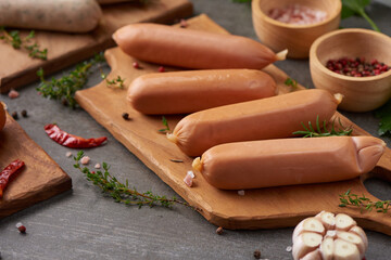 Fresh raw sausages and ingredients for cooking. Classic boiled meat pork sausages on chopping board with pepper, rosemary, herbs and spices. Selective focus, Top view with copy space on stone table