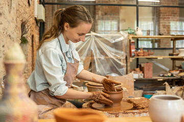 Female potter sculpts a clay pot. The sculptor works with clay on a potter's wheel and at a table