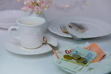 close-up of a white plate for money, euro banknotes and coins, Restaurant bill, cup of coffee, delicate pink flowers, dishes with food, calculator, concept of tip money, change of the waiter