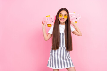 Photo of happy nice attractive cute little girl hold longboard look empty space smile isolated on pink color background