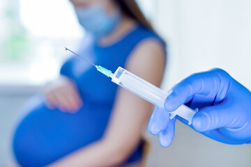 Pregnant Vaccination. Pregnant Woman In Face Mask Getting Vaccinated in Clinic. Doctor Giving Corona Virus Vaccine Injection Patient. Covid-19 Flu Protection. Selective focus. Syringe close up