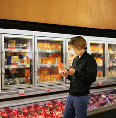 Young man shopping in supermarket, reading product information.