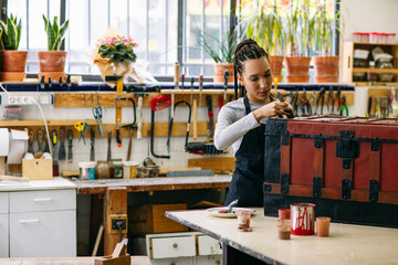 Craftswoman varnishing wooden chest in workshop 