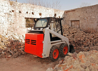 A bobcat skid steer loader in a partially demolished derelict old stone Italian farm building in...