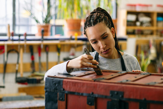 Craftswoman varnishing wooden chest in workshop 