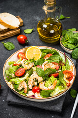 Shrimp salad with green leaves, tomatoes, octopus and ollive oil at black table.