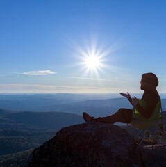 girl tourist meditating sitting on a rock against the backdrop of a sunset, a mountain valley and the sun with rays.  Travel camping and adventure lifestyle concept.