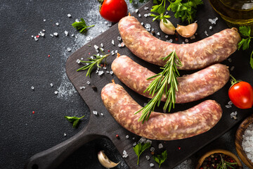 Bratwurst or sausages on cutting board with spices at black table. Top view with copy space.
