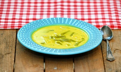 Cream soup with pineapple and green bean in blue plate on wooden background.