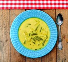 Cream soup with pineapple and green bean in blue plate on wooden background.