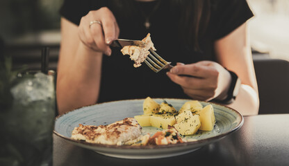 woman hand holding fork and knife eat chicken breast meat with potato in a plate