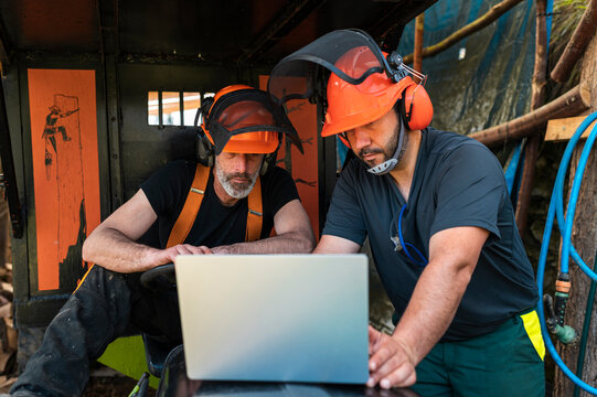 Focused lumberjacks using laptop together at sawmill 