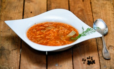 Red tomato soup with pork meat and cabbage in white plate on wooden background.