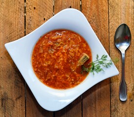 Red tomato soup with pork meat and cabbage in white plate on wooden background.