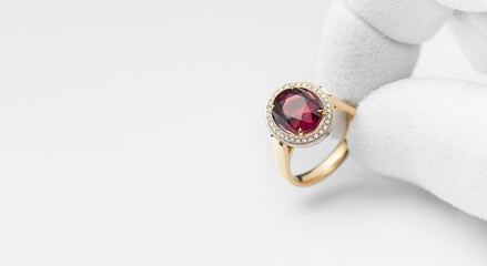 Jeweler examining ruby or rhodolite ring in workshop, closeup view. Gold ring with rhodolite and diamonds in the hand of a jeweler. Copy free space on left. Concept for jeweler or shop - obrazy, fototapety, plakaty