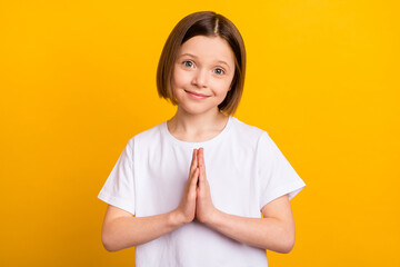 Photo portrait small schoolgirl smiling keeping hands together asking wish isolated vibrant yellow color background