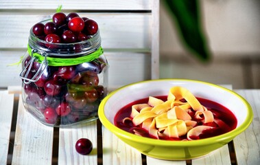 Red soup with cherries and pasta on a white and green plate on wooden background.