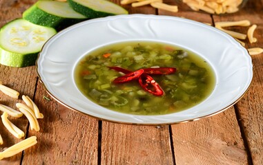 Green soup with zucchini, chilli papper, pasta and green bean on a white plate on wooden background.