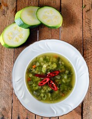 Green soup with zucchini, chilli papper and green bean on a white plate on wooden background.