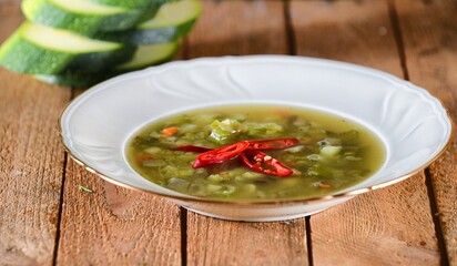 Green soup with zucchini, chilli papper and green bean on a white plate on wooden background.