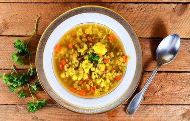 Green soup with carrot, parsley, cauliflower on a white plate on wooden background.