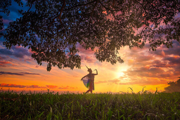 Silhouette Manohra women dance and tree with sunset in South of Thailand.