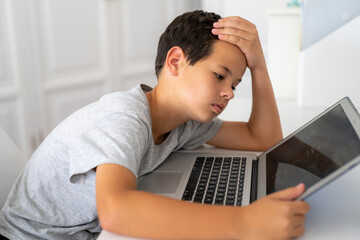 Serious young boy in bedroom using laptop