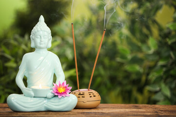 Buddha statue with burning candle and lotus flower near incense sticks on wooden table. Space for...