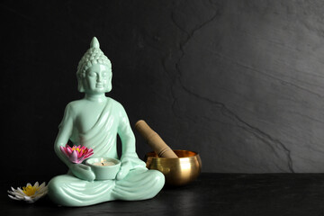 Buddha statue with burning candle, lotus flowers and singing bowl on black table. Space for text