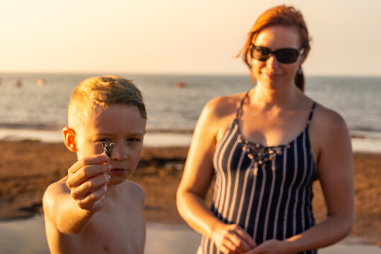 Boy Holding Up Rock Exploring Red Sand Beach on PEI at Sunset