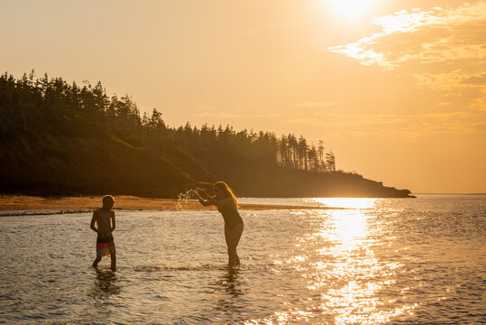 Woman Splashing Boy on Red Sand Beach on PEI at Sunset