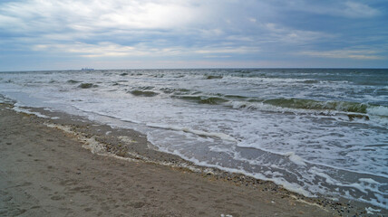 Black sea with waves and white foam under the blue sky in the clouds on a spring cloudy day