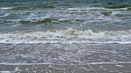 Black sea with waves and white foam under the blue sky in the clouds on a spring cloudy day