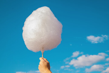 A man's hand holds cotton candy against a blue sky. White cotton wool like a cloud.