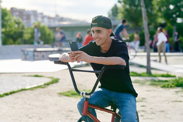Smiling young man on a BMX checking his phone