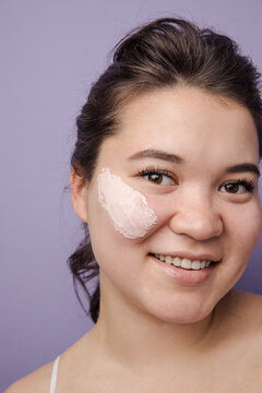 Beautiful east asian model with pink clay mask on her face smiling
