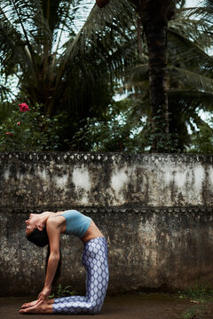 A Young Woman In Camel Pose In Front Of An Old Wall Outside