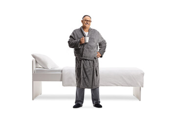 Full length portrait of a mature man wearing a robe and holding a cup in front of a bed